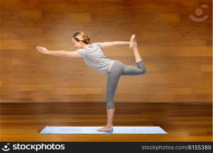 fitness, sport, people and healthy lifestyle concept - woman making yoga in lord of the dance pose on mat over wooden room background