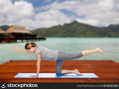 fitness, sport, people and healthy lifestyle concept - woman making yoga in balancing table pose on wooden pier over island beach and bungalow background. woman making yoga in balancing table pose outdoors
