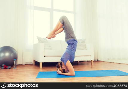 fitness, sport, people and healthy lifestyle concept - woman making yoga in headstand pose on mat. woman making yoga in headstand pose on mat