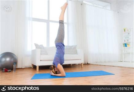 fitness, sport, people and healthy lifestyle concept - woman making yoga in headstand pose on mat