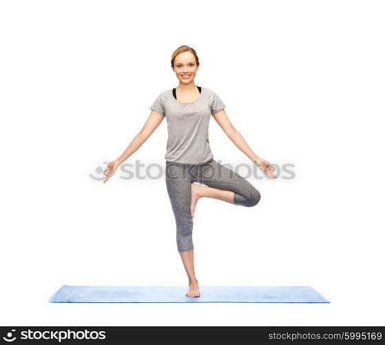 fitness, sport, people and healthy lifestyle concept - woman making yoga in tree pose on mat