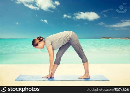 fitness, sport, people and healthy lifestyle concept - woman making yoga intense stretch pose on mat over beach background. woman making yoga intense stretch pose on mat