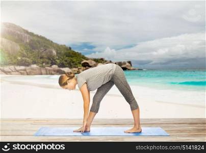 fitness, sport, people and healthy lifestyle concept - woman making yoga intense stretch pose on mat over exotic tropical beach background. woman making yoga intense stretch pose on beach