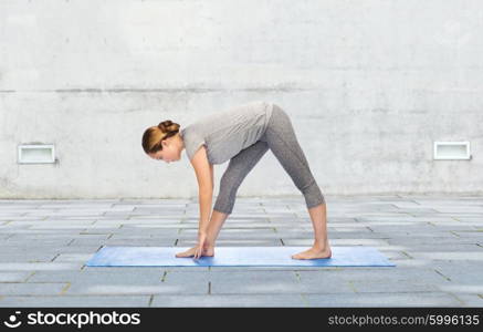 fitness, sport, people and healthy lifestyle concept - woman making yoga intense stretch pose on mat over urban street background