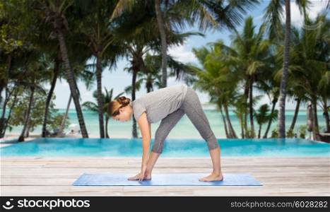 fitness, sport, people and healthy lifestyle concept - woman making yoga intense stretch pose on mat over hotel resort pool on tropical beach background