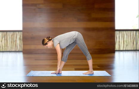 fitness, sport, people and healthy lifestyle concept - woman making yoga intense stretch pose on mat over wooden gym background