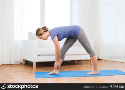 fitness, sport, people and healthy lifestyle concept - woman making yoga intense stretch pose on mat