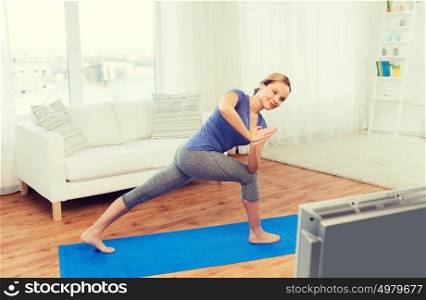 fitness, sport, people and healthy lifestyle concept - woman making yoga low angle lunge pose on mat and watching tv lesson. woman making yoga low angle lunge pose on mat