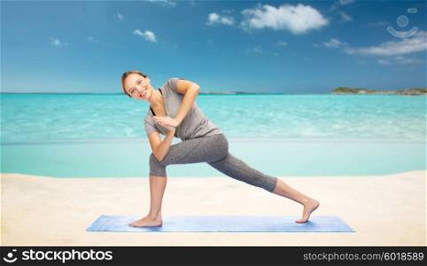 fitness, sport, people and healthy lifestyle concept - woman making yoga low angle lunge pose on mat over sea and sky background