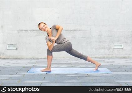 fitness, sport, people and healthy lifestyle concept - woman making yoga low angle lunge pose on mat over urban street background
