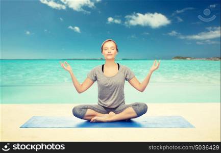 fitness, sport, people and healthy lifestyle concept - woman making yoga meditation in lotus pose on mat over beach background. woman making yoga meditation in lotus pose on mat