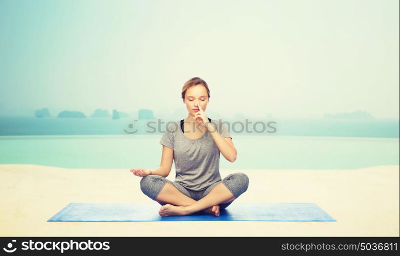 fitness, sport, people and healthy lifestyle concept - woman making yoga meditation in lotus pose on mat over infinity edge pool at hotel resort background. woman making yoga meditation in lotus pose on mat