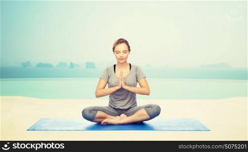 fitness, sport, people and healthy lifestyle concept - woman making yoga meditation in lotus pose on mat over infinity edge pool at hotel resort background. woman making yoga meditation in lotus pose on mat