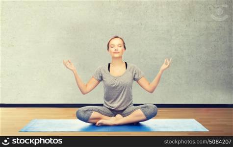 fitness, sport, people and healthy lifestyle concept - woman making yoga meditation in lotus pose on mat over gym room background. woman making yoga meditation in lotus pose on mat. woman making yoga meditation in lotus pose on mat