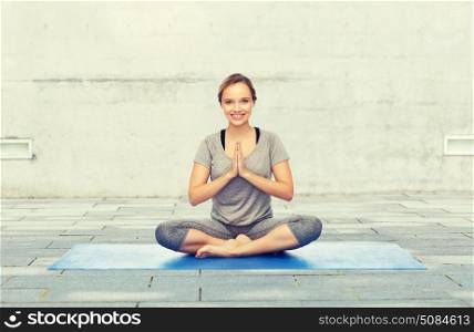 fitness, sport, people and healthy lifestyle concept - woman making yoga meditation in lotus pose on mat over urban street background. woman making yoga meditation in lotus pose on mat. woman making yoga meditation in lotus pose on mat