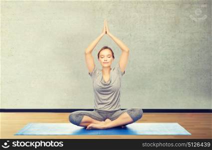fitness, sport, people and healthy lifestyle concept - woman making yoga meditation in lotus pose on mat over gym room background. woman making yoga meditation in lotus pose on mat
