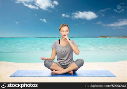 fitness, sport, people and healthy lifestyle concept - woman making yoga meditation in lotus pose on mat over sea and sky background