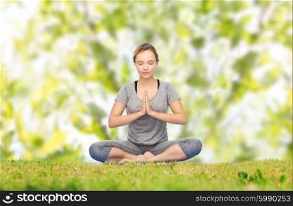 fitness, sport, people and healthy lifestyle concept - woman making yoga meditation in lotus pose on mat over green natural background