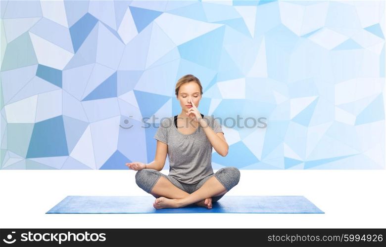 fitness, sport, people and healthy lifestyle concept - woman making yoga meditation in lotus pose on mat over blue polygonal background