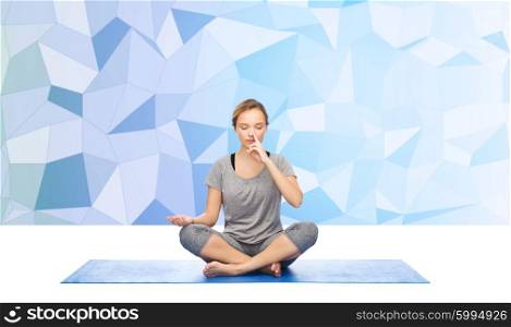 fitness, sport, people and healthy lifestyle concept - woman making yoga meditation in lotus pose on mat over blue polygonal background