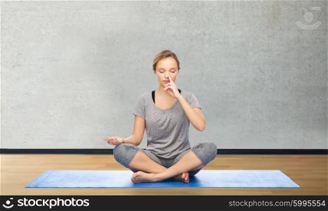 fitness, sport, people and healthy lifestyle concept - woman making yoga meditation in lotus pose on mat over room or gym background