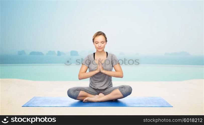 fitness, sport, people and healthy lifestyle concept - woman making yoga meditation in lotus pose on mat over infinity edge pool at hotel resort background