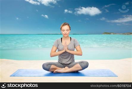 fitness, sport, people and healthy lifestyle concept - woman making yoga meditation in lotus pose on mat over sea and sky background