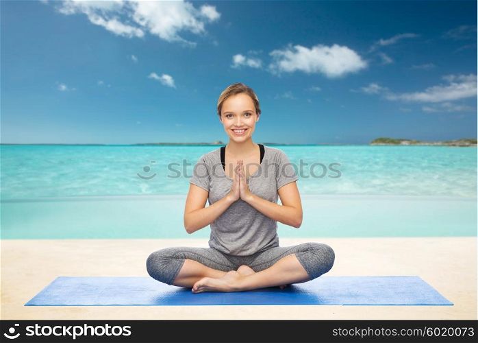fitness, sport, people and healthy lifestyle concept - woman making yoga meditation in lotus pose on mat over beach background