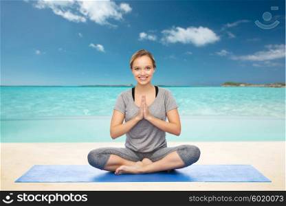fitness, sport, people and healthy lifestyle concept - woman making yoga meditation in lotus pose on mat over beach background