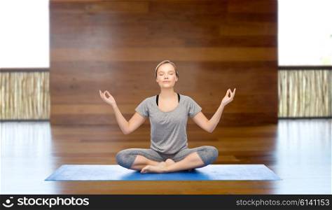 fitness, sport, people and healthy lifestyle concept - woman making yoga meditation in lotus pose on mat over wooden gym background