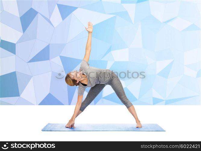 fitness, sport, people and healthy lifestyle concept - woman making yoga triangle pose on mat over low poly background