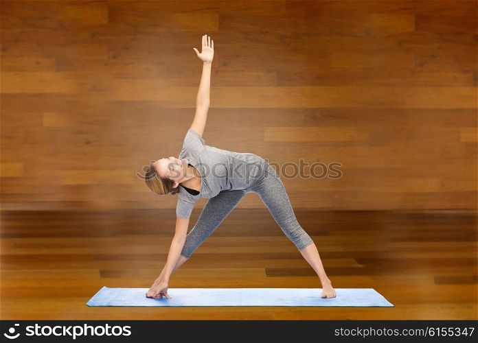 fitness, sport, people and healthy lifestyle concept - woman making yoga triangle pose on mat over wooden room background