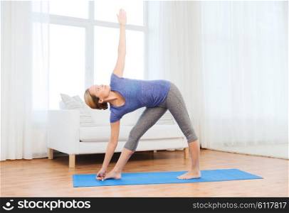fitness, sport, people and healthy lifestyle concept - woman making yoga triangle pose on mat