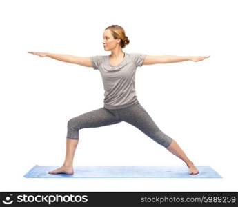 fitness, sport, people and healthy lifestyle concept - woman making yoga warrior pose on mat