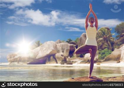fitness, sport, people and healthy lifestyle concept - woman meditating in yoga tree pose over exotic beach background from back . woman meditating in yoga tree pose over beach