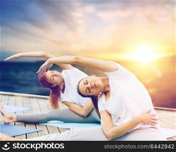 fitness, sport, people and healthy lifestyle concept - women doing yoga exercises outdoors on wooden pier over sea background. women doing yoga exercises outdoors
