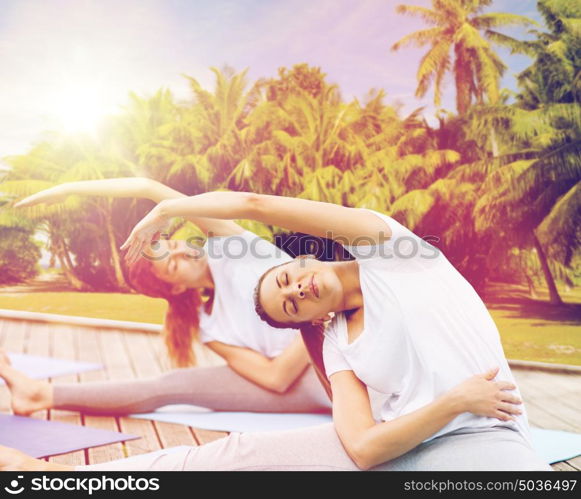 fitness, sport, people and healthy lifestyle concept - women making yoga exercises outdoors over exotic natural background with palm trees. women making yoga exercises outdoors