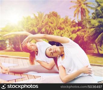 fitness, sport, people and healthy lifestyle concept - women making yoga exercises outdoors over exotic natural background with palm trees. women making yoga exercises outdoors