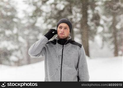 fitness, sport, people and healthy lifestyle concept - young man with earphones listening to music in winter forest