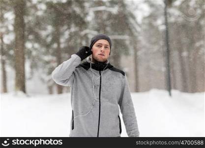 fitness, sport, people and healthy lifestyle concept - young man with earphones listening to music in winter forest