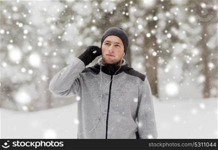 fitness, sport, people and healthy lifestyle concept - young man with earphones listening to music in winter forest. sports man with earphones in winter forest