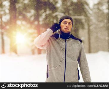 fitness, sport, people and healthy lifestyle concept - young man with earphones listening to music in winter forest. sports man with earphones in winter forest