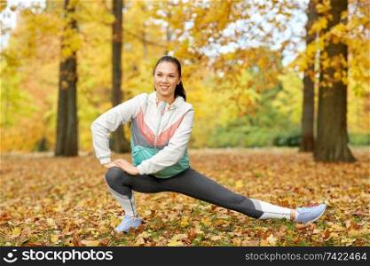 fitness, sport, people and healthy lifestyle concept - young woman stretching leg at autumn park. young woman doing sports at autumn park