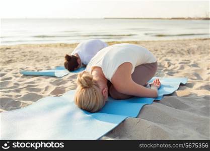 fitness, sport, people and lifestyle concept - close up of couple making yoga exercises on mats outdoors