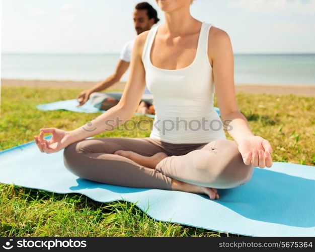 fitness, sport, people and lifestyle concept - close up of couple making yoga exercises sitting on mats outdoors