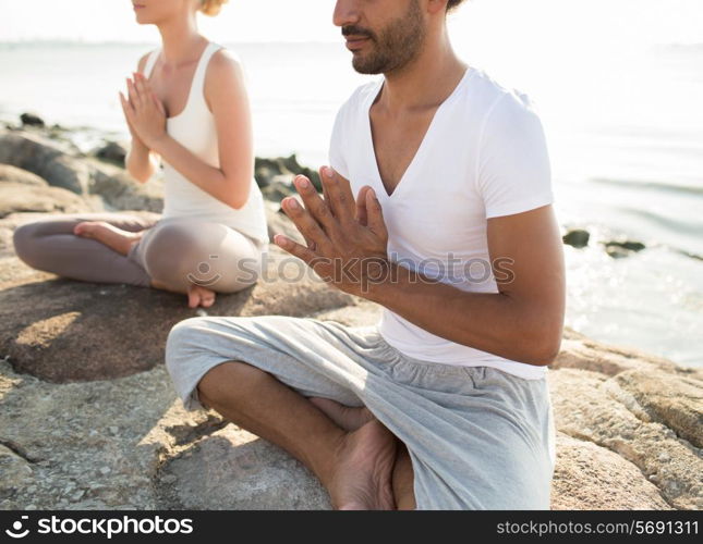 fitness, sport, people and lifestyle concept - close up of couple making yoga exercises sitting on pier outdoors