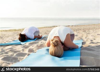 fitness, sport, people and lifestyle concept - close up of couple making yoga exercises on mats outdoors