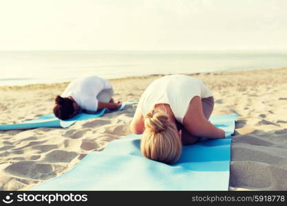 fitness, sport, people and lifestyle concept - close up of couple making yoga exercises on mats outdoors