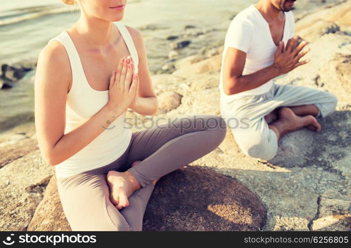 fitness, sport, people and lifestyle concept - close up of couple making yoga exercises sitting on pier outdoors