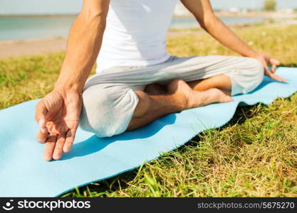 fitness, sport, people and lifestyle concept - close up of man making yoga exercises on mat outdoors